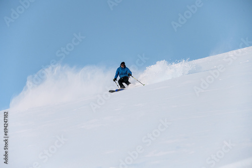 Skier with poles in his hands goes down a snowy slope