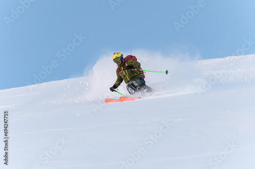 Male skier in a ski suit, a helmet with goggles is going down a snowy slope