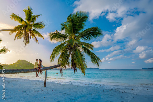 a couple of men and a woman sitting on a palm tree at Anse Volbert Beach Praslin Seychelles watching the sunset. couple hugging together on the beach photo