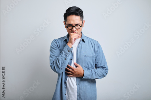 Portrait of young asian man wearing denim and glasses coughing with sore throat