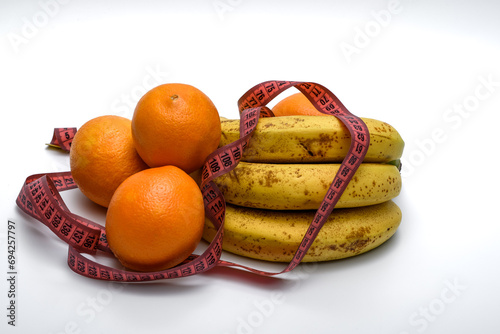 Owoce banany i pomarańcze leżą owinięte miara krawiecka na białym tle