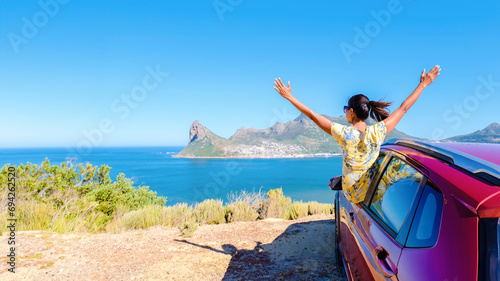 woman outside a car window with hands up, a car at Chapman's Peak Drive in Cape Town South Africa looking out over the ocean. women on a road trip at the garden route South Africa with a renal car photo