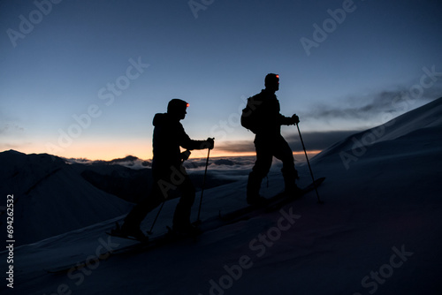 Silhouettes of two skiers with flashlights on their foreheads climbing the mountain slope photo