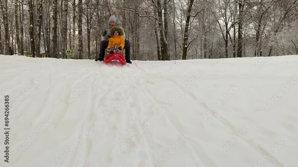 Mother with small child sledding in winter park. Family winter activities outdoors.