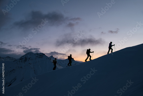 Silhouettes of four skiers on the highest point of the mountain against the background of the mountain peaks in the fog © fesenko