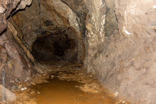 Old abandoned gold mine underground tunnel with rusty water lake. Dangerous tunnel full of dirt and rusty equipment.