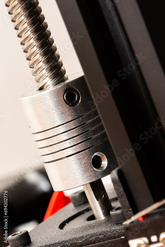 Detail of a flexible coupling connecting a motor shaft and a rod of a 3D printer. Vertical photo.