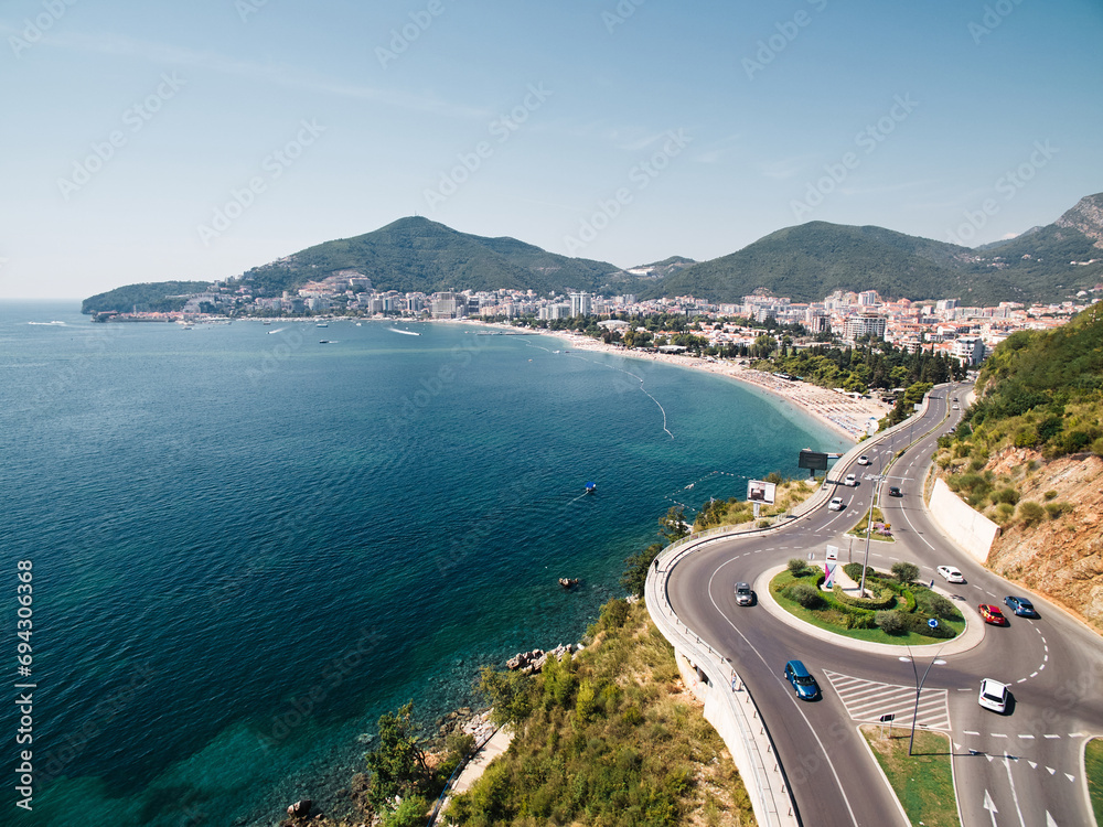 Highway with a circular turn over the sea at the foot of the mountains. Budva, Montenegro. Drone