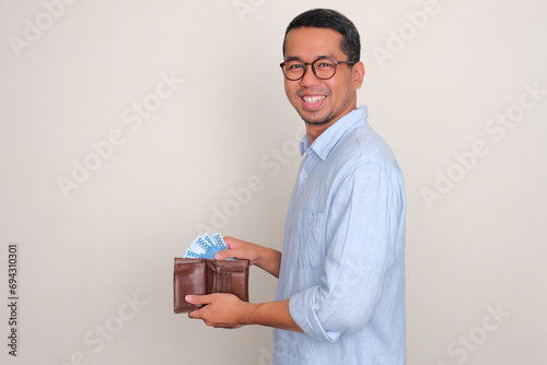 Side view of Asian man smiling happy while taking out money from inside his wallet photo