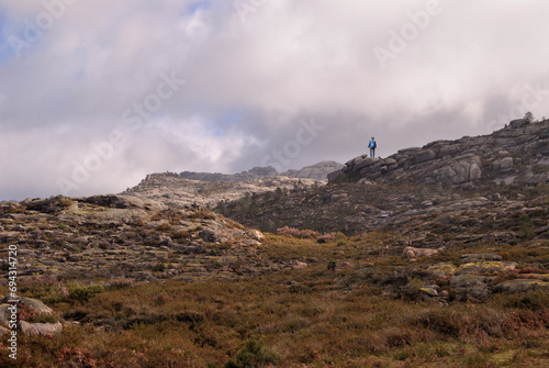 Mountain range landscape with a person hiking, standing on top of a rock contemplating nature