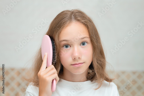 A pretty little girl with big blue eyes and a comb in her hand. The child combs unruly hair. Cute little girl is playing with a hairbrush.