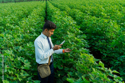 Indian agronomist or banker using tablet or phone at agriculture field.