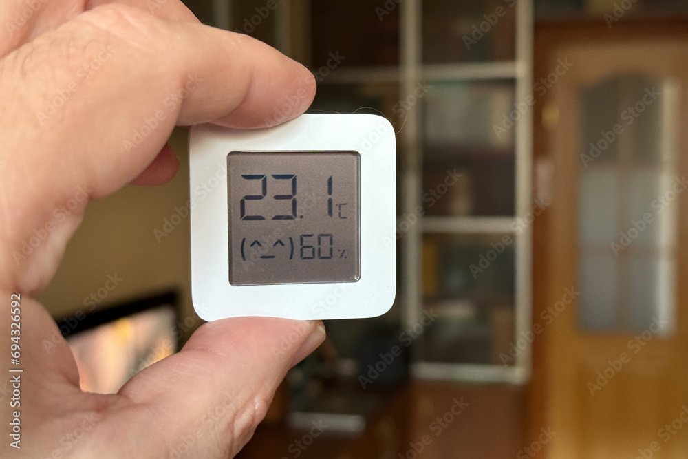 Close-up of a man holding a hygrometer. Temperature and humidity readings in a room at home - obrazy, fototapety, plakaty 