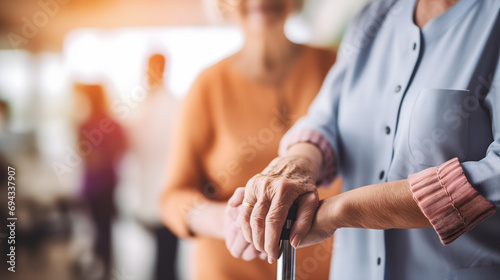 Les mains d'une personne âgée s'appuyant sur une canne, tenue par une aide-soignante dans une maison de retraite. photo