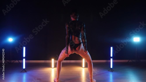 Sexy woman dances a seductive dance. A dancer girl with a big ass dances erotically in a dark hall. Twerk, high heels, striptease, photo