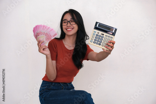 Cheerful Asian woman sitting and showing some cash money and a calculator in both hands photo