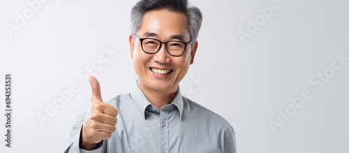Approving middle-aged Asian freelancer man happily works on laptop and gives positive feedback at office. photo