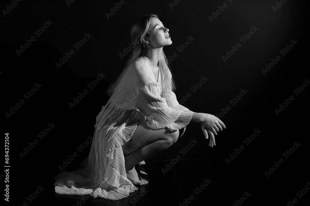 Low key black and white portrait of young pretty woman in vintage white dress sitting on the floor Low key black and white portrait of young pretty woman in vintage white dress sitting on the floor