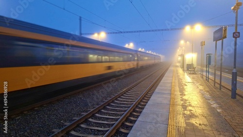Passage of a passenger train to the station in fog. Night train passing through the station. Concept of passenger rail transport. Night passenger train in fog