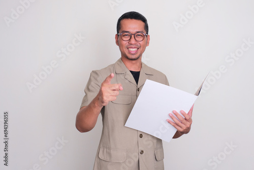Indonesia government worker smiling and pointing at the camera while holding a document file photo