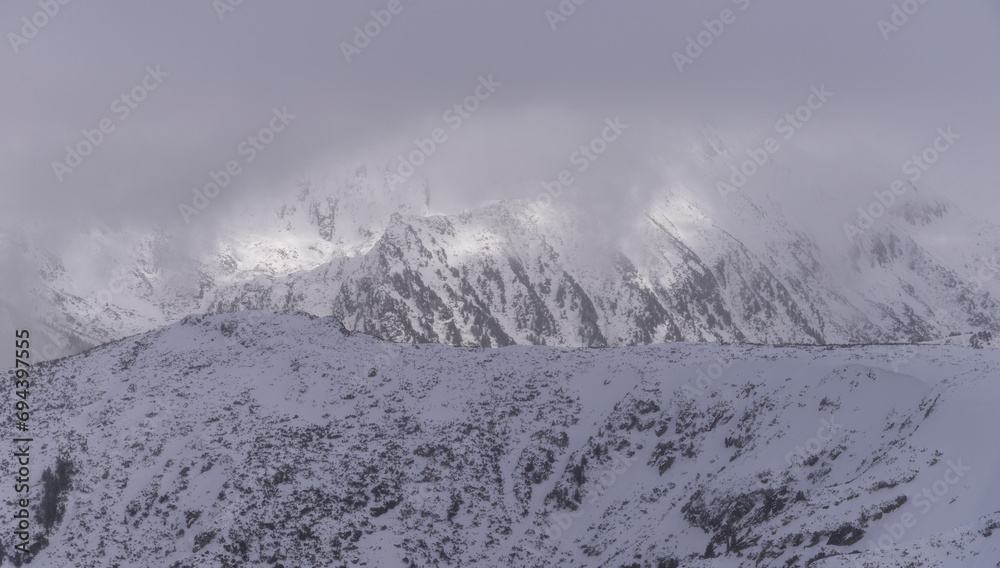 Obraz premium The white snowy peaks of Pirin covered with snow and fog. Snowy weather conditions for winter sports and tourism. Bansko Alpine Ski Resort, Bulgaria.