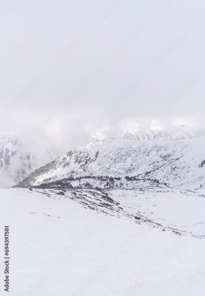 Obraz premium The white snowy peaks of Pirin covered with snow and fog. Snowy weather conditions for winter sports and tourism. Bansko Alpine Ski Resort, Bulgaria.
