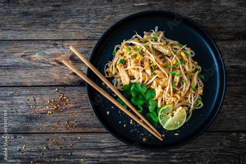 Pad Thai with chicken nuggets and rice noodles in peanut and tamarind sauce on wooden table 