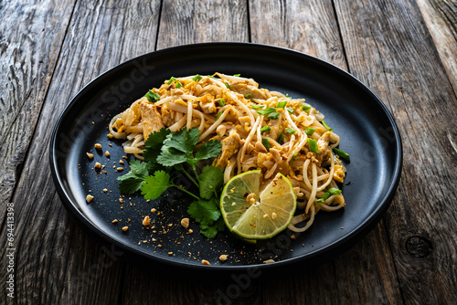 Pad Thai with chicken nuggets and rice noodles in peanut and tamarind sauce on wooden table
 photo