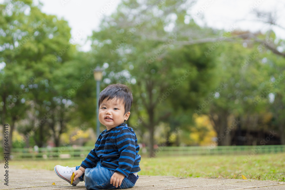 Fototapeta premium 屋外の自然あふれる公園内で楽しそうに笑顔で遊ぶファーストシューズを履いた1歳の幼児