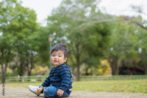 屋外の自然あふれる公園内で楽しそうに笑顔で遊ぶファーストシューズを履いた1歳の幼児