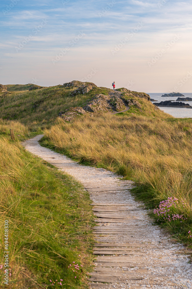 A path, leading through grassy sand dunes, to a ridge overlooking the ocean. it is evening and the scene is bathed in golden light. Angelsey, Wales A path, leading through grassy sand dunes, to a ridge overlooking the ocean. it is evening and the scene is bathed in golden light. Angelsey, Wales