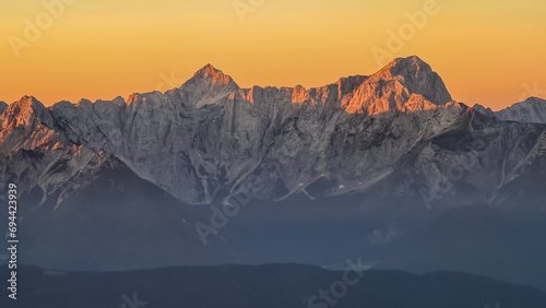 Panoramic sunrise view from summit Dobratsch on Julian Alps and Karawanks in Austria, Europe. Silhouette of endless mountain ranges with orange and pink colors of sky. Jagged sharp peaks and valleys photo
