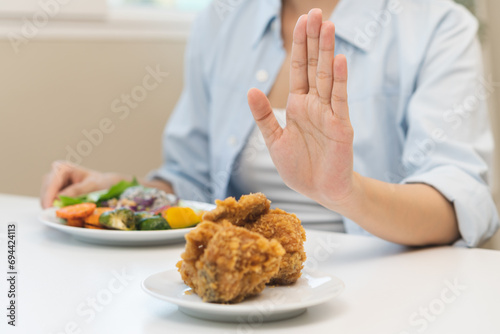 Diet, Dieting asian young woman hand push out, reject fried chicken on plate, deny to eat fast, junk food choose green vegetable salad, girl eat low fat for good healthy, getting weight loss people. photo