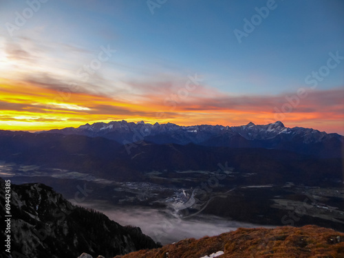 Panoramic sunrise view from summit Dobratsch on Julian Alps and Karawanks in Austria, Europe. Silhouette of endless mountain ranges with orange and pink colors of sky. Jagged sharp peaks and valleys
