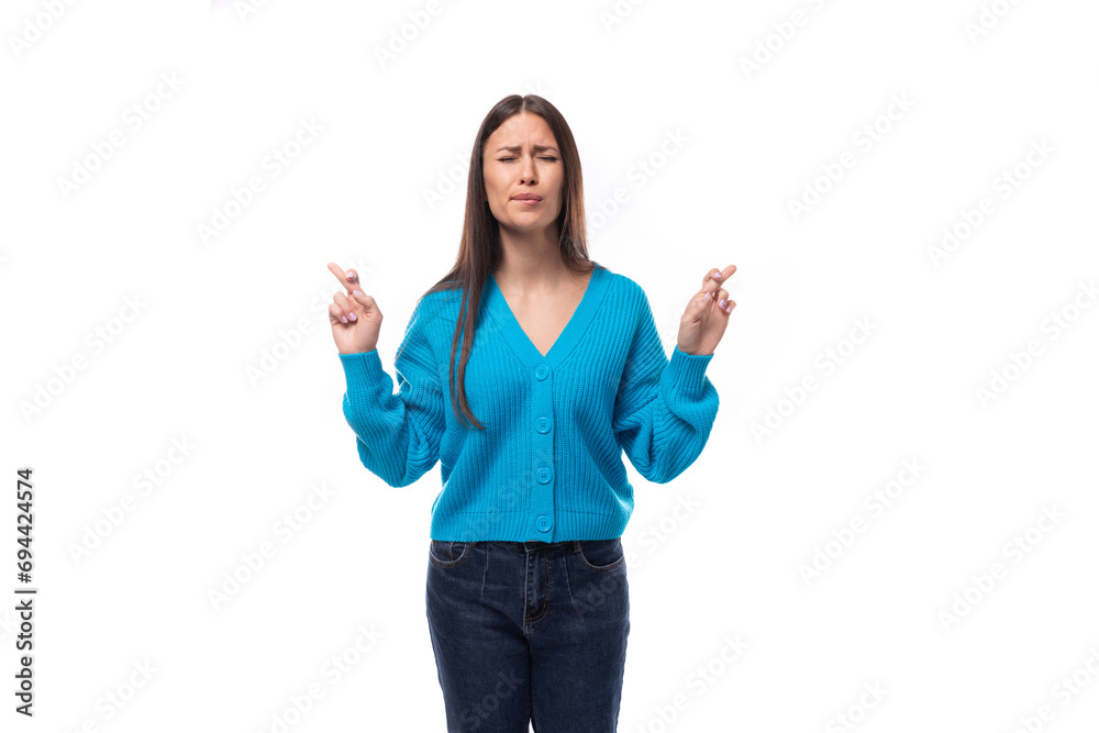 surprised young brunette lady dressed in blue casual buttoned cardigan crossed her fingers in anticipation of good news