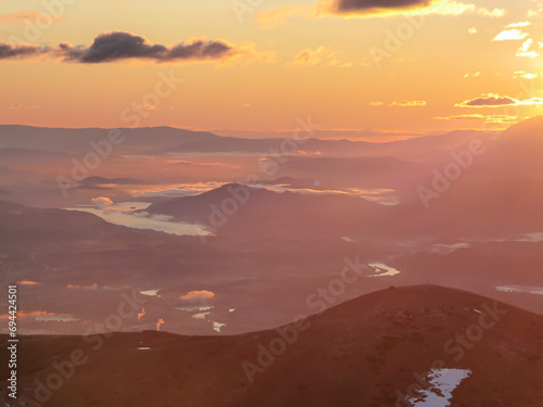 Panoramic sunrise view from Dobratsch on Julian Alps and Karawanks in Austria, Europe. Silhouette of endless mountain ranges. Lake Woerthersee (lake Woerth) surrounded by mysterious haze and fog