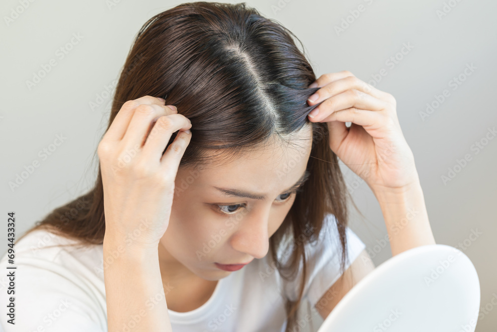 Fototapeta premium Damaged Hair, face serious asian young woman worry looking at scalp in mirror, hand in break into front hair loss, thin problem symptom at home. Health care shampoo beauty, isolated on background.