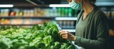Masked woman shopping for fresh greens in a supermarket during the pandemic for a healthy plant-based diet amid Covid-19 quarantine prep.