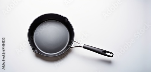  a frying pan on a white surface with a black handle and a black handle on the bottom of the frying pan.