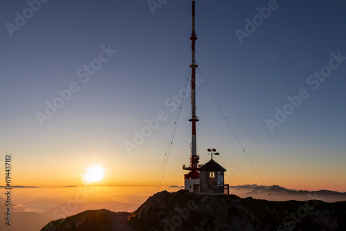 Scenic view of radio tower on top of mountain peak Dobratsch during sunrise on Villacher Alps, Carinthia, Austria, Europe. Panoramic view of Julian Alps at golden hour. Endless high mountain ranges photo