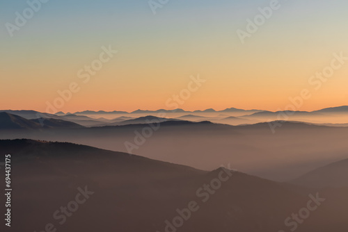 Panoramic sunrise view from Dobratsch on High Tauern and Nocky Alps in Austria, Europe. Silhouette of endless mountain ranges covered by mystical fog in valley. Jagged sharp peaks and alpine landscape