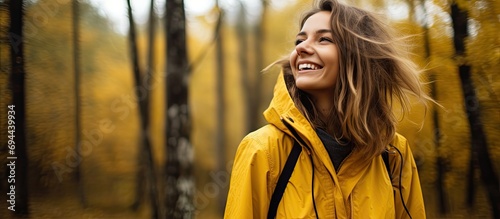 Joyful woman hiker with yellow coat enjoys autumn forest. Active lifestyle in park.