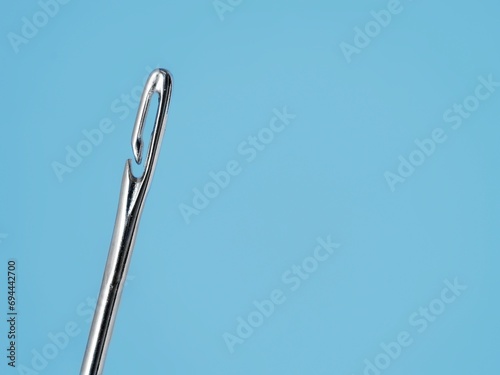 Silver blind eye needle for easy threading closeup on a blue background and copy space