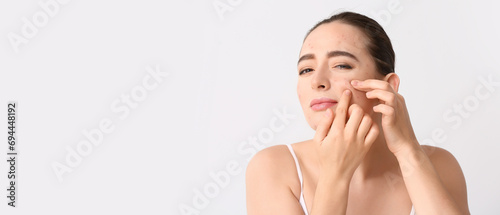 Young woman with acne problem squishing pimples on light background with space for text photo