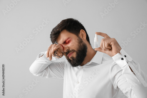 Young man with eyeglasses and eye drops on grey background photo