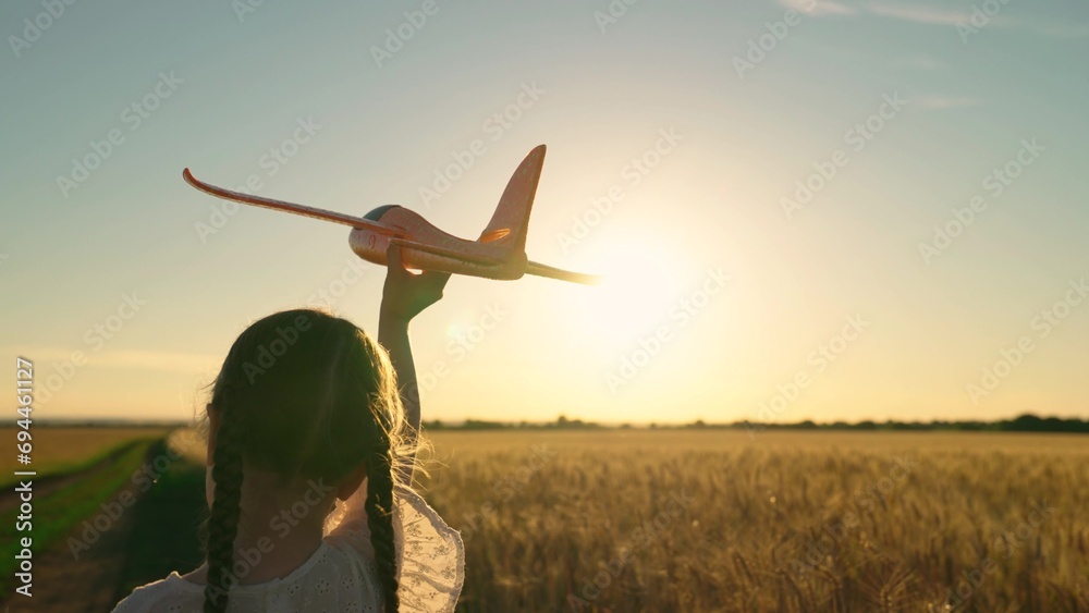 Little girl child wants to become pilot and astronaut. Kid aviator dreams of flying and becoming pilot. Slow motion. Happy girl runs with toy airplane on field in sunset light. Child play toy airplane - obrazy, fototapety, plakaty 