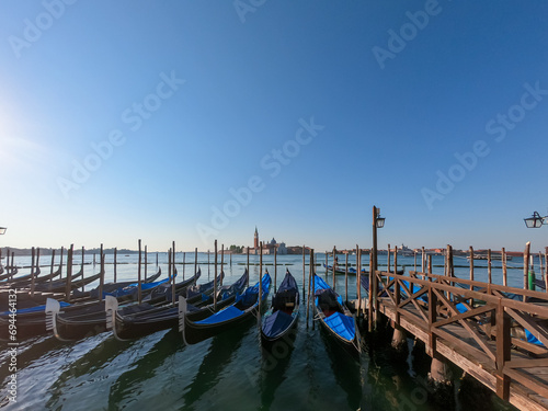 Group of gondolas moored by Saint Mark square in city of Venice, Veneto, Northern Italy, Europe. Scenic view of San Giorgio di Maggiore church in background. Romantic vacation in the Venetian Lagoon © Chris
