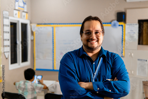 Portrait of latin american male teacher with arms crossed smiling in the class at school
