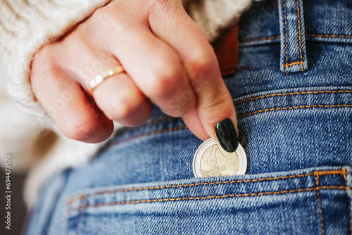 Pocket money background. Euro coin in rear pocket. Woman in blue jeans. Girl in trousers. American style fashion. Hand reaching for money. Coin in fingers. Shopping change coins. photo