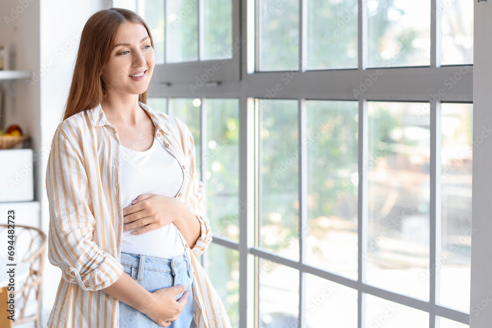 Young pregnant woman looking in window at home Young pregnant woman looking in window at home